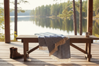 Blue chevron cotton throw blanket with cream fringe draped over a wooden bench by a lake